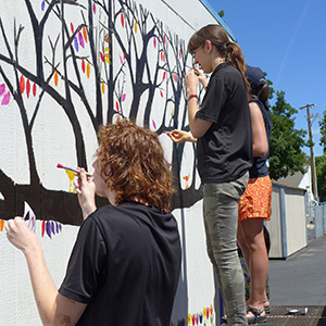students painting a tree on a building wall
